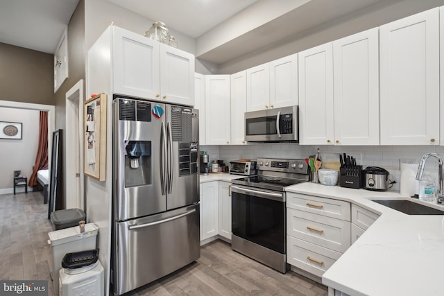 kitchen with stainless steel appliances, sink, white cabinets, and backsplash