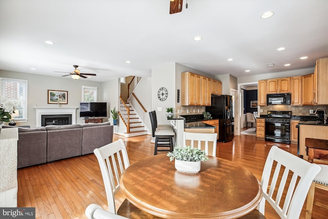 dining space featuring light wood-style flooring, recessed lighting, a ceiling fan, stairway, and a glass covered fireplace