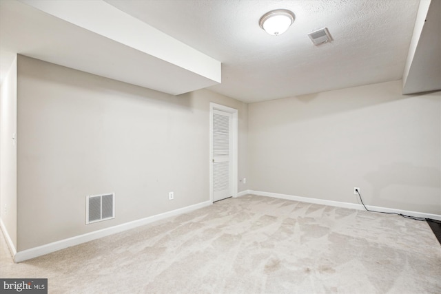 finished below grade area with baseboards, visible vents, a textured ceiling, and light colored carpet