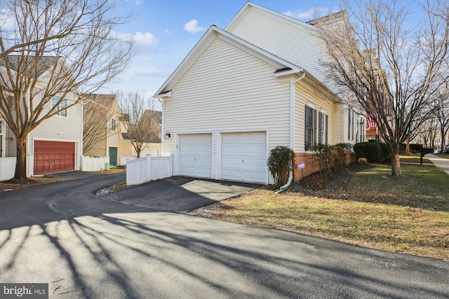 view of side of home featuring driveway, an attached garage, fence, and brick siding