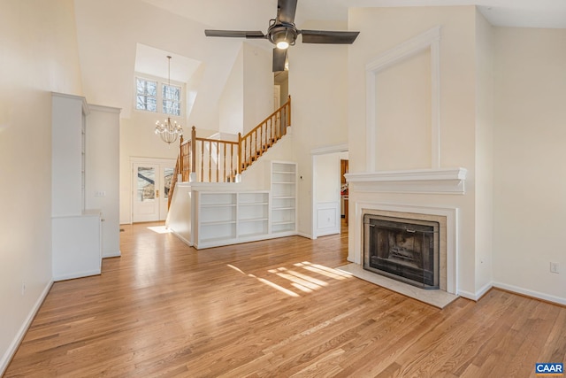 unfurnished living room featuring a towering ceiling, ceiling fan with notable chandelier, and light wood-type flooring