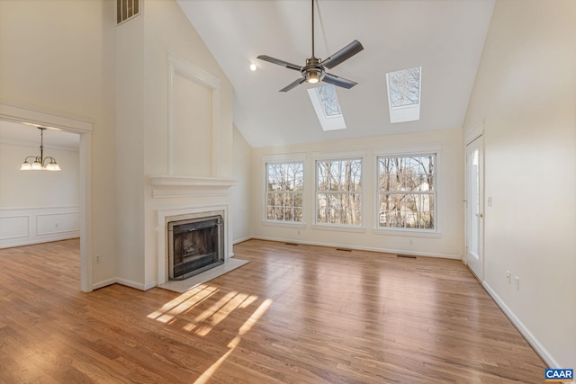 unfurnished living room with ceiling fan with notable chandelier, a high end fireplace, high vaulted ceiling, and light wood-type flooring