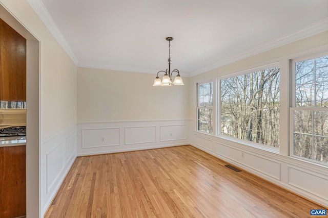 unfurnished dining area with ornamental molding, a healthy amount of sunlight, a chandelier, and light hardwood / wood-style floors