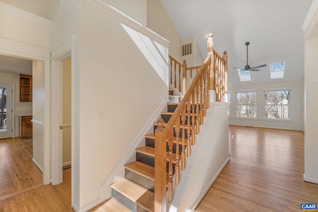 stairway with hardwood / wood-style flooring, ceiling fan, a skylight, and high vaulted ceiling