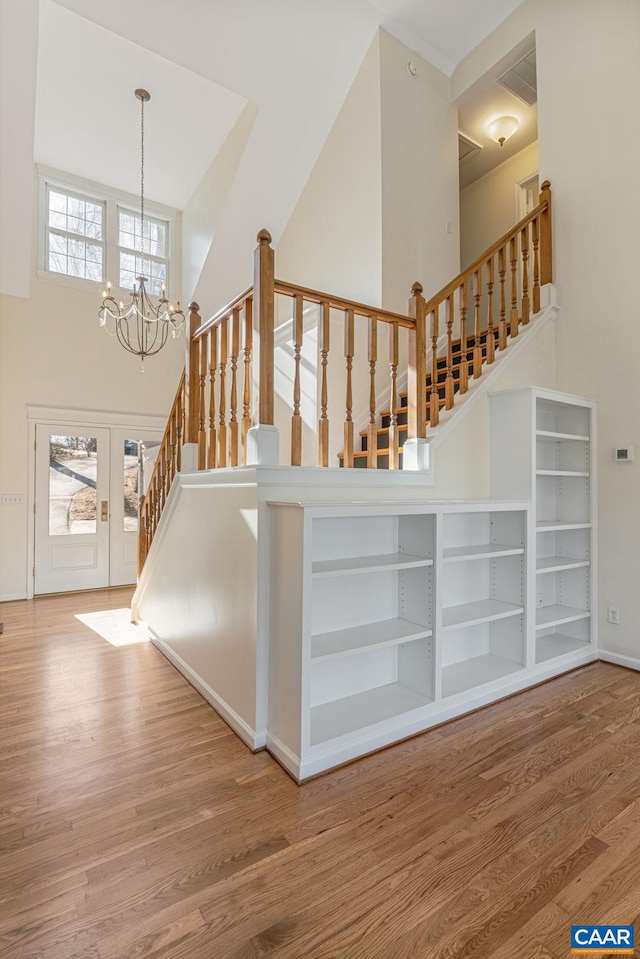 staircase featuring french doors, wood-type flooring, a chandelier, and a high ceiling