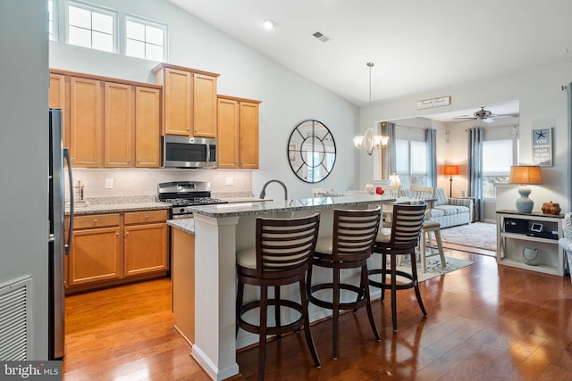 kitchen with a breakfast bar, light stone counters, decorative light fixtures, stainless steel appliances, and a kitchen island with sink