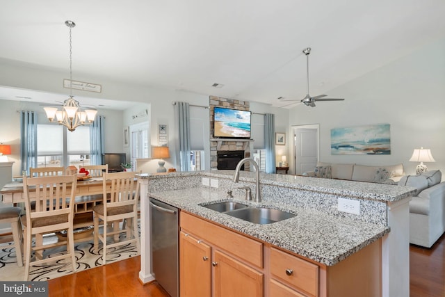 kitchen with sink, dark hardwood / wood-style floors, light stone counters, a stone fireplace, and stainless steel dishwasher