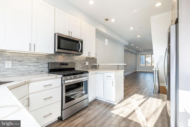 kitchen with appliances with stainless steel finishes, white cabinetry, hanging light fixtures, backsplash, and kitchen peninsula