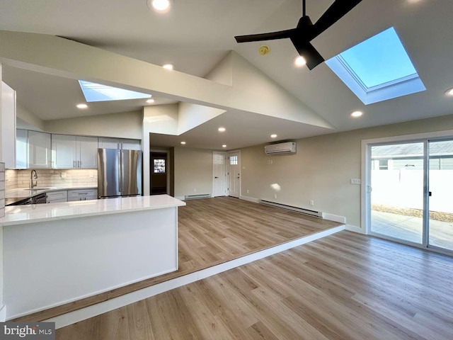 kitchen with an AC wall unit, vaulted ceiling with skylight, stainless steel refrigerator, white cabinetry, and baseboard heating