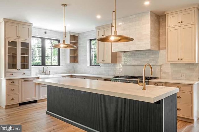 kitchen with sink, light hardwood / wood-style flooring, hanging light fixtures, a kitchen island with sink, and cream cabinetry