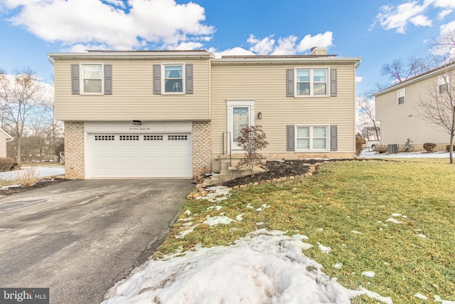 bi-level home featuring a garage, cooling unit, and a front lawn