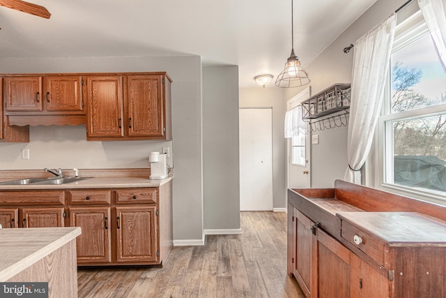 kitchen with hanging light fixtures, plenty of natural light, sink, and light wood-type flooring