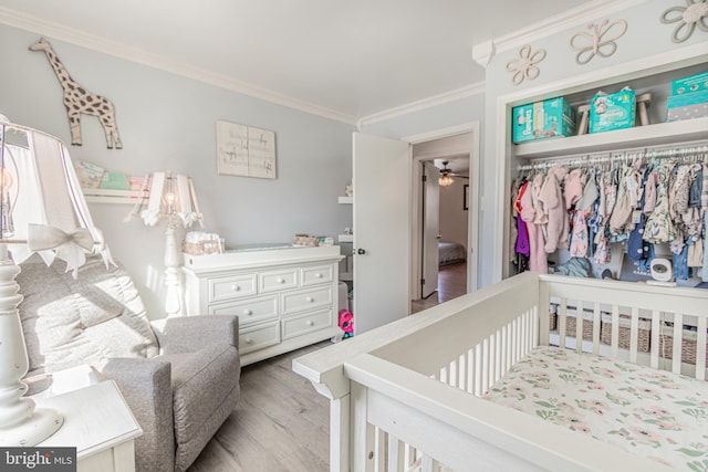 bedroom with crown molding, a nursery area, light hardwood / wood-style floors, and a closet