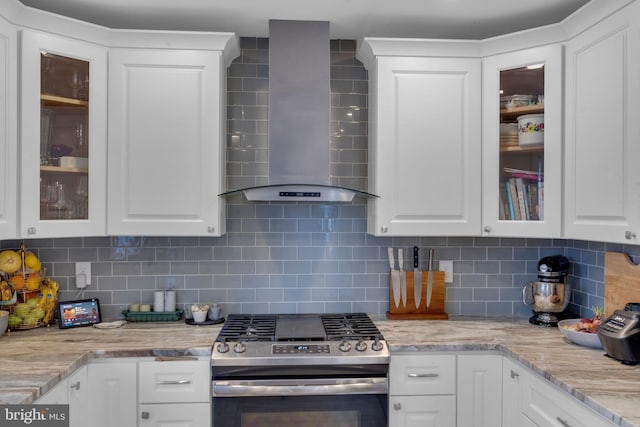 kitchen with tasteful backsplash, white cabinets, gas stove, light stone countertops, and wall chimney exhaust hood