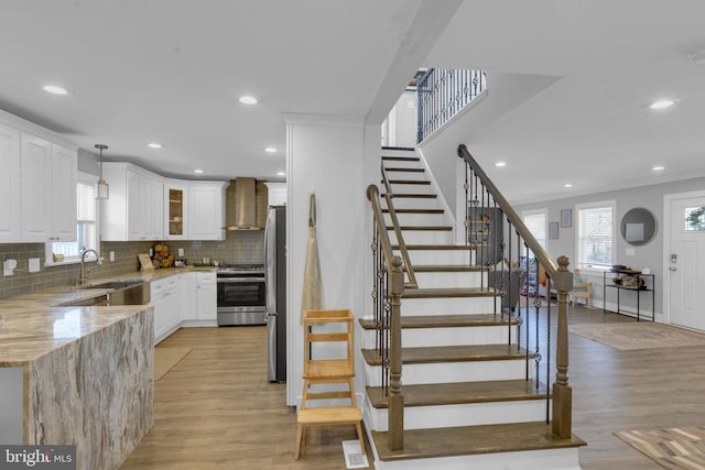 kitchen featuring appliances with stainless steel finishes, decorative light fixtures, white cabinetry, light stone counters, and wall chimney exhaust hood