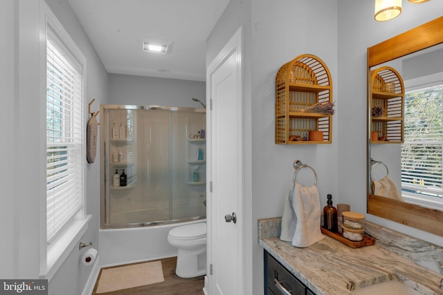 full bathroom with hardwood / wood-style flooring, vanity, combined bath / shower with glass door, and toilet