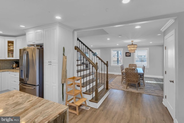 kitchen featuring stainless steel fridge, white cabinetry, backsplash, light stone counters, and light hardwood / wood-style floors