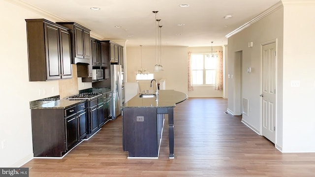 kitchen featuring a breakfast bar, wood-type flooring, hanging light fixtures, crown molding, and a center island with sink