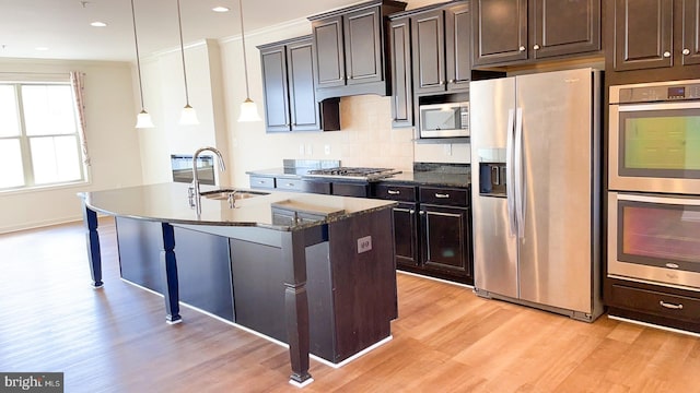 kitchen with pendant lighting, an island with sink, sink, dark stone counters, and stainless steel appliances