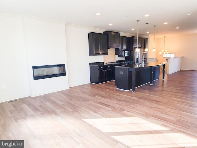 kitchen with a breakfast bar area, hanging light fixtures, a center island with sink, a notable chandelier, and stainless steel appliances