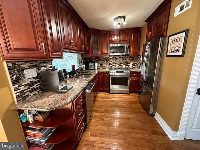 kitchen with stone countertops, tasteful backsplash, sink, stainless steel appliances, and light wood-type flooring