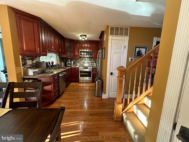 kitchen with stone countertops, sink, backsplash, dark hardwood / wood-style flooring, and stainless steel appliances