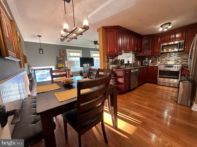 dining space featuring wood-type flooring, ornamental molding, and ceiling fan with notable chandelier