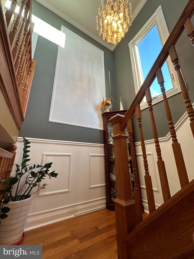 staircase with crown molding, wood-type flooring, and a chandelier