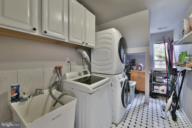 laundry room featuring cabinets, stacked washer and clothes dryer, and sink