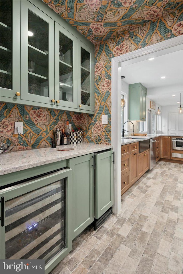 bar with wine cooler, light stone counters, green cabinetry, decorative light fixtures, and stainless steel appliances