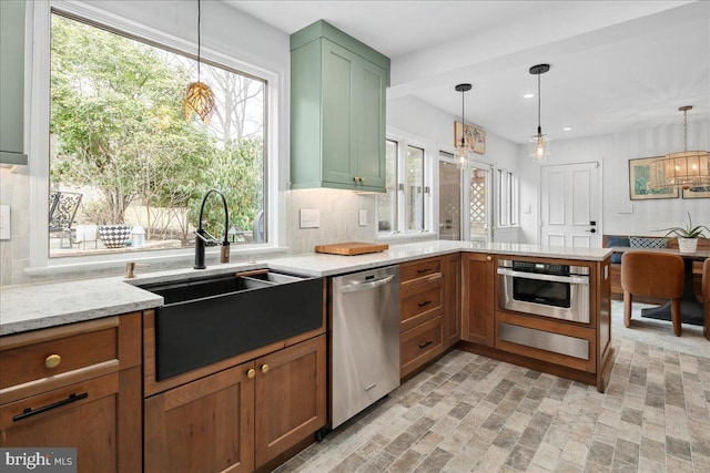 kitchen featuring sink, hanging light fixtures, stainless steel appliances, light stone countertops, and decorative backsplash