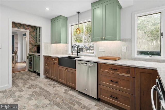 kitchen featuring decorative light fixtures, dishwasher, sink, green cabinets, and light stone counters