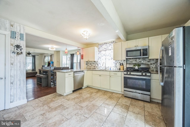 kitchen with sink, hanging light fixtures, stainless steel appliances, kitchen peninsula, and beamed ceiling