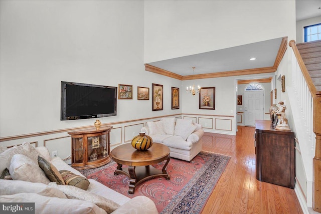 living room with crown molding, a towering ceiling, a notable chandelier, and light hardwood / wood-style floors