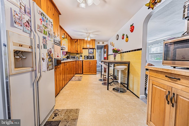 kitchen featuring white fridge with ice dispenser, tile walls, and ceiling fan