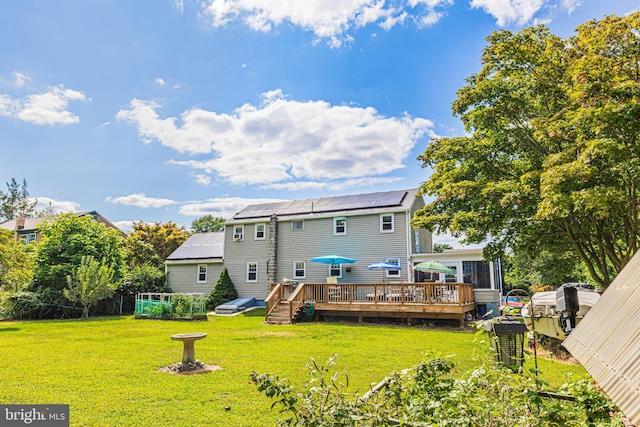 rear view of house with a wooden deck, a lawn, and solar panels