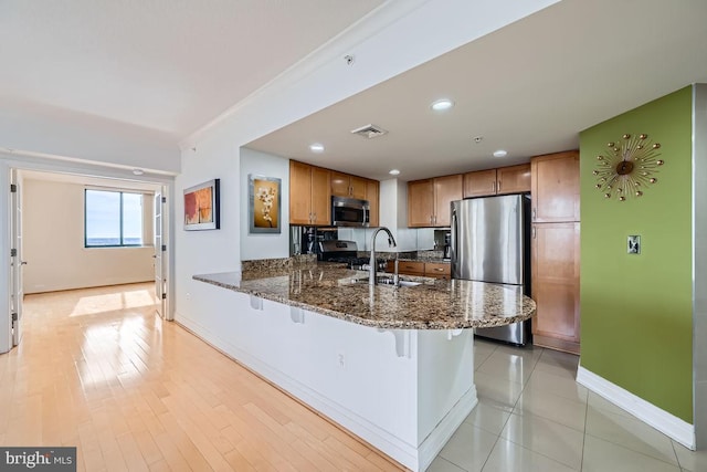 kitchen featuring a breakfast bar, sink, dark stone counters, kitchen peninsula, and stainless steel appliances