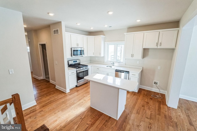 kitchen with a kitchen island, appliances with stainless steel finishes, sink, white cabinets, and light hardwood / wood-style floors