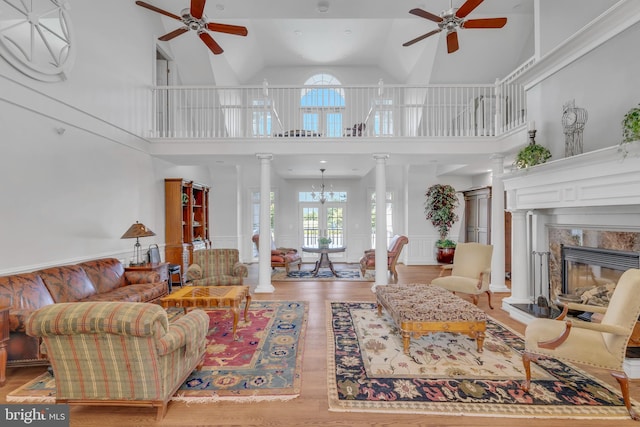 living area featuring wood finished floors, decorative columns, ceiling fan with notable chandelier, and a premium fireplace