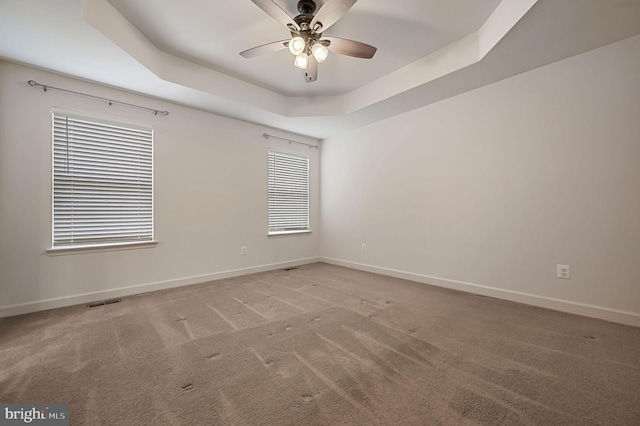 carpeted empty room with a raised ceiling and ceiling fan