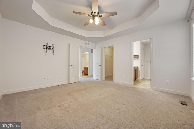 unfurnished bedroom featuring connected bathroom, a spacious closet, light colored carpet, a raised ceiling, and a closet