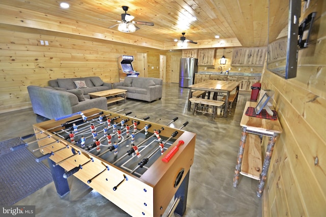 rec room with ceiling fan, wood walls, a tray ceiling, and wooden ceiling