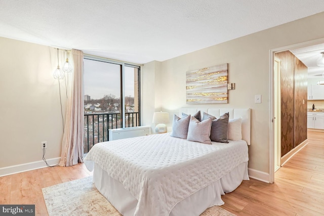 bedroom featuring floor to ceiling windows, access to exterior, a textured ceiling, and light hardwood / wood-style flooring