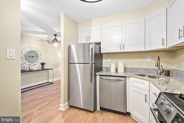 kitchen with appliances with stainless steel finishes, sink, white cabinets, and light stone counters