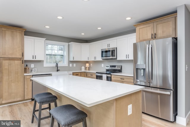 kitchen featuring white cabinetry, a kitchen breakfast bar, a center island, light hardwood / wood-style floors, and stainless steel appliances