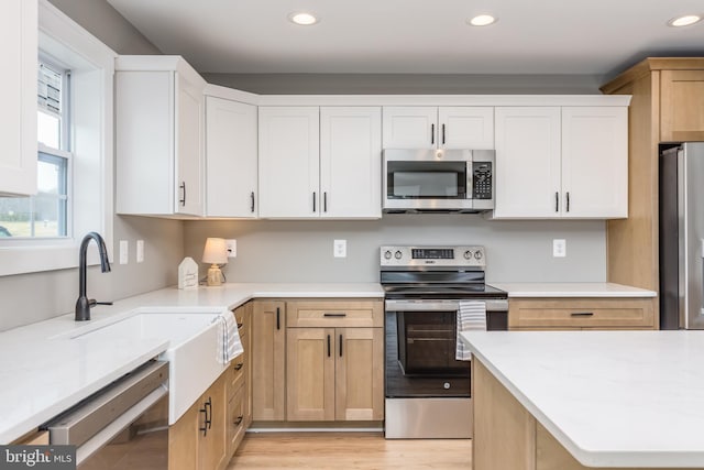 kitchen featuring white cabinetry, sink, light stone counters, light hardwood / wood-style floors, and stainless steel appliances