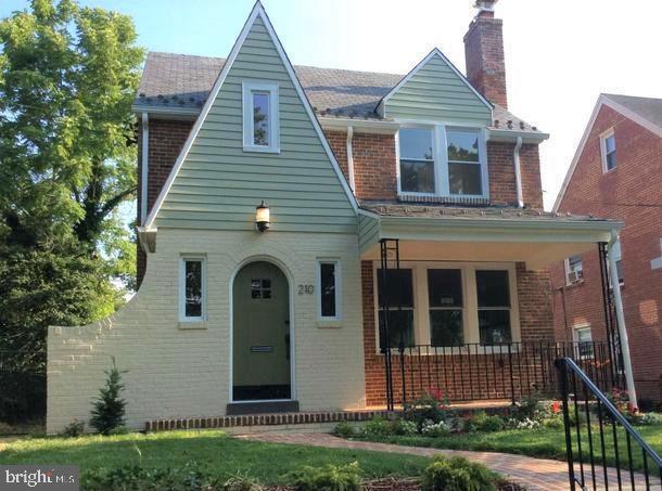 english style home with a front yard, covered porch, brick siding, and a chimney