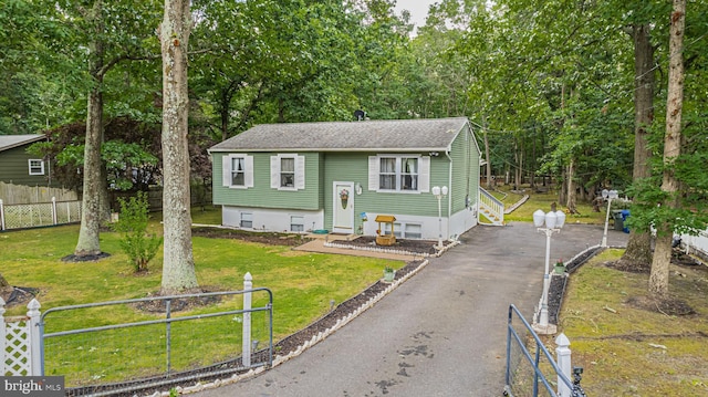 bi-level home featuring driveway, entry steps, a fenced front yard, roof with shingles, and a front lawn