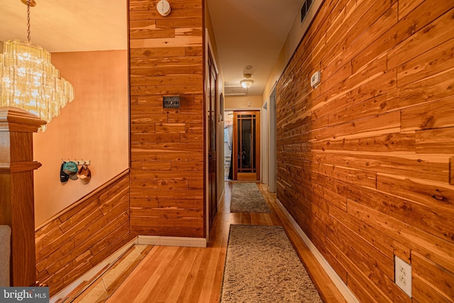 hallway featuring light wood-type flooring, wooden walls, and visible vents