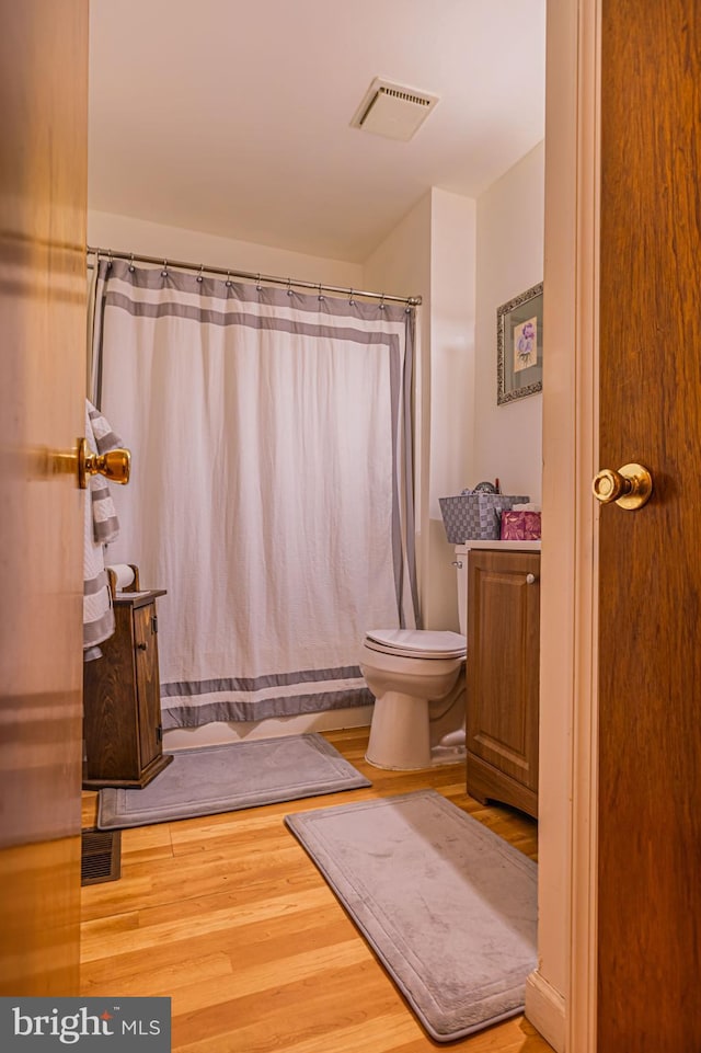 full bath with toilet, curtained shower, wood finished floors, and visible vents